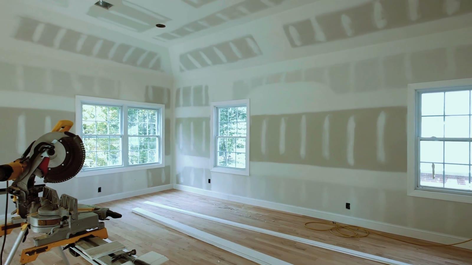 Room stripped back for carpentry: drywall taped, new floor down, mitre saw set up