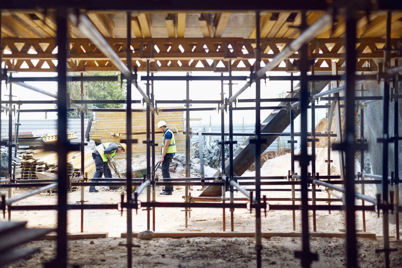Two construction workers on site, seen through scaffolding